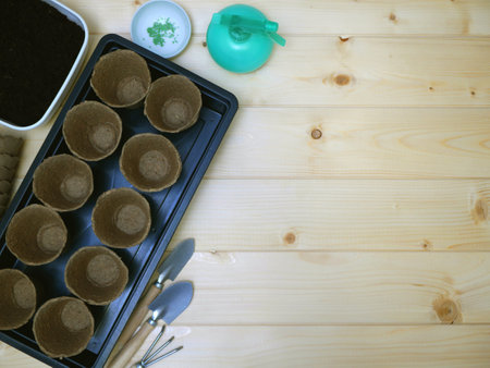 Top view on small garden tools accessories. Flatlay with peat pots, spray, black plastic box, seeds, ground, small shovels and rake on wooden desk.の写真素材