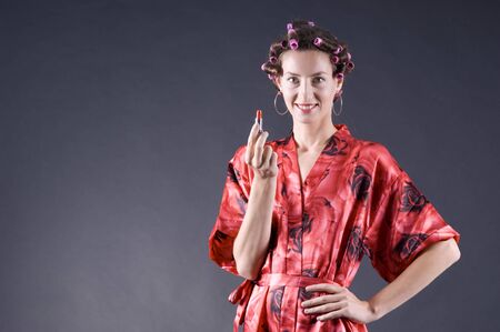 Beautiful girl in a red robe home paints her lips on a gray background closeupの写真素材