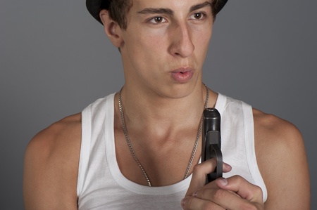 A young man with a gun in his hand on a gray background in the studioの写真素材