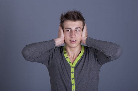Young guy shut their ears with their hands on a gray background in the studio