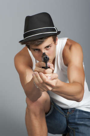 A young man with a gun in his hand on a gray background in the studio, focus on the hands with a gunの写真素材
