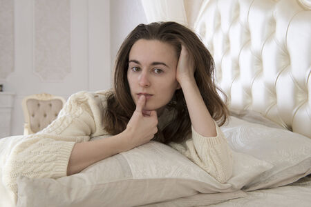 Girl in a light sweater is resting on the large bedの写真素材