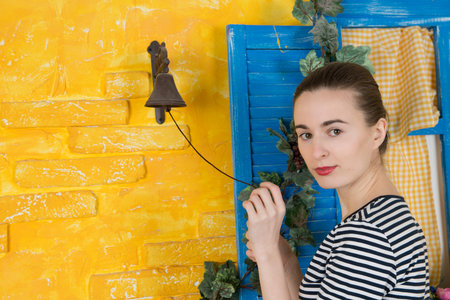 Young attractive woman rings the bell on the wall of a village house