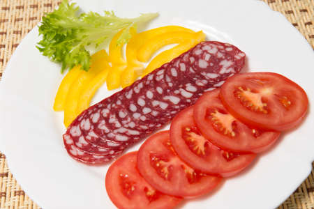 Dry salami and tomatoes on a white plate, closeupの写真素材