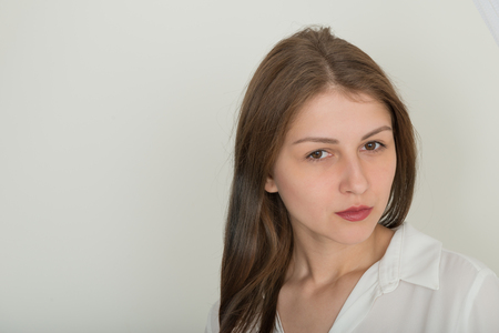 Portrait of a cute girl with beautiful long straight hair in a white blouse on a light backgroundの写真素材