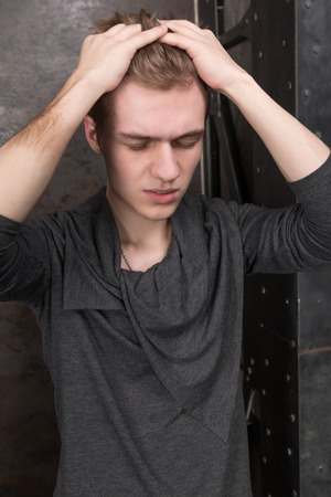 Young man with a headache, eyes closed, arms wrapped around his headの写真素材