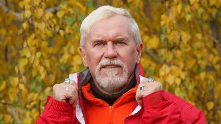 Happy beautiful elderly man with gray hair in orange sportswear on a background of autumn trees with yellow leavesの写真素材