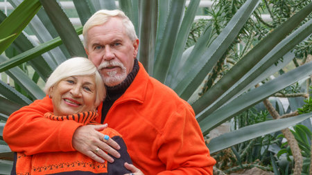 Happy beautiful elderly married couple with gray hair in orange sportswear against a background of...