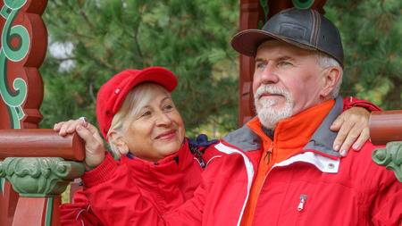 Happy beautiful elderly married couple with gray hair in red sportswear on a background of autumn trees with yellow leavesの写真素材