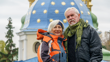 Beautiful elderly couple with gray hair in sports autumn jackets against the background of the dome of the Orthodox churchの写真素材