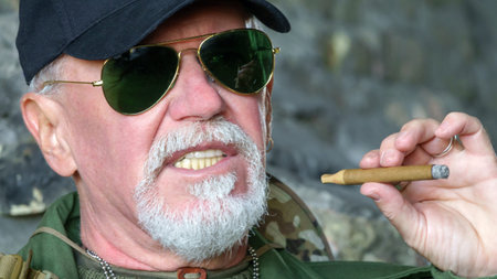 Portrait of confident elderly man wearing protective clothing in sunglasses with a cigar against the background of old concrete wallsの写真素材