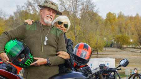 Portrait of a cheerful elderly couple with a motorcycle on the background of an autumn landscape