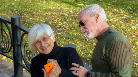 Portrait of a loving elderly couple with a smartphone in hand on the background of the autumn city...