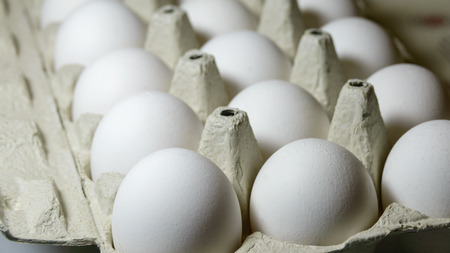 Fresh raw chicken eggs in white color in a special cardboard tray closeupの写真素材