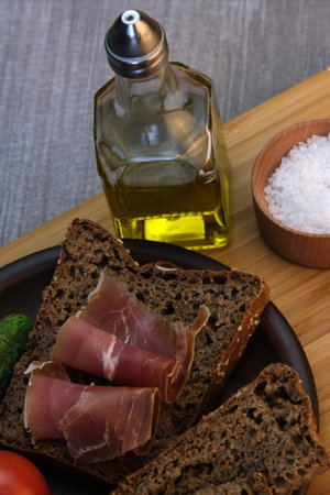 Snack with homemade rye bread and dried pork on a brown clay plate close-up