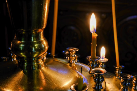 Thin funeral candles burn in front of holy images in an Orthodox Christian church close-up