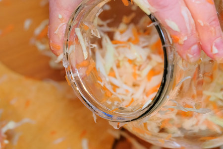 Shredder cabbage for pickling with carrots and spices in a glass jar in a city apartment, close-up