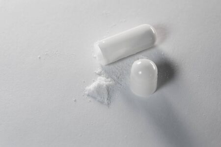 White gelatin soluble capsules with medicinal powder on a white background close-up macro photoの写真素材