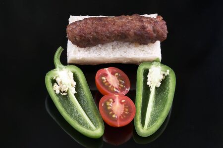 Grilled sausage civapchi rests on white bread with vegetables close-up on a black background macro photographyの写真素材