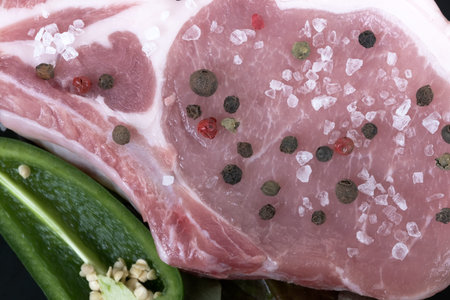 Raw pork loin on the bone close-up with vegetables, herbs and spicy spices on a black background macro photoの写真素材