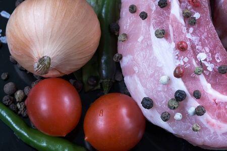 Raw pork fat brisket closeup with vegetables, herbs and spicy spices on a black background macro photoの写真素材