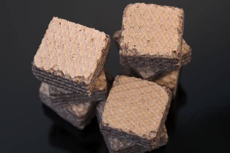 Small square pieces of sweet waffles with chocolate filling against black background close-up macro photoの写真素材