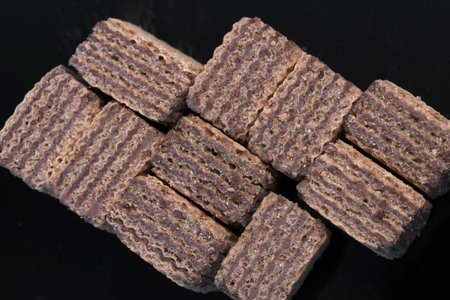 Small square pieces of sweet waffles with chocolate filling against black background close-up macro...