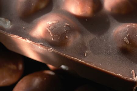 A bar of dark dark chocolate with whole hazelnuts closeup grocery background macro photographyの写真素材