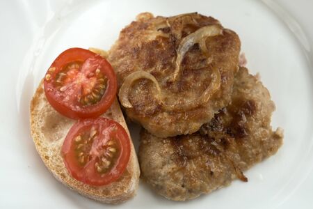 Tasty fresh hot meat cutlet from a mix of beef, pork and chicken fried with onions close-up with a slice of white bread and a tomato on a white plate macro photoの写真素材