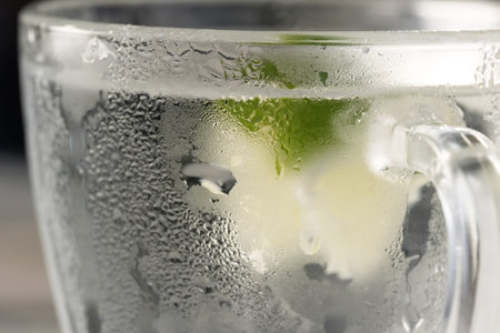 Refreshing lemonade with slices of lime with ice in a transparent sweaty glass cup close-up macro...
