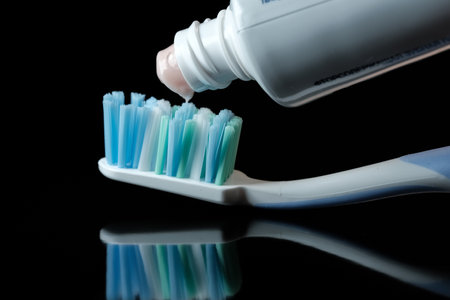Toothbrush with light pink toothpaste on black background close-up macro photographyの写真素材