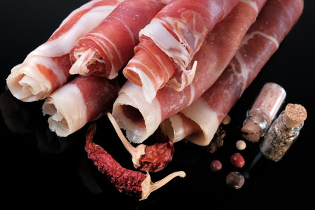 Cured pork jamon cut into thin layers and rolled into tubes lies on a black background close-up macro photographyの写真素材