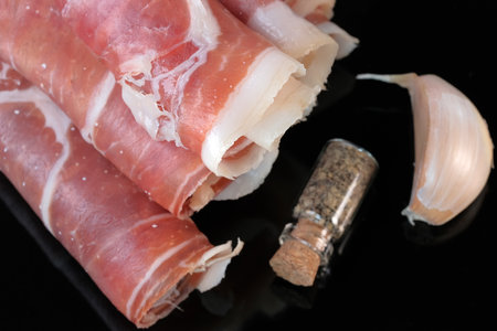 Cured pork jamon cut into thin layers and rolled into tubes lies on a black background close-up macro photographyの写真素材