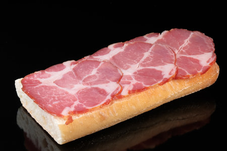 A sandwich with raw smoked sausage on a black background close-upの写真素材