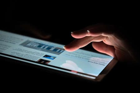 Hand of a woman who is viewing the news on a tablet close-up on a black backgroundのeditorial素材