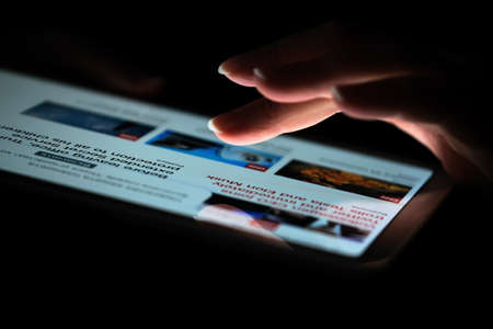 Hand of a woman who is viewing the news on a tablet close-up on a black backgroundのeditorial素材