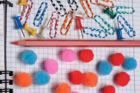 Stationery composition with colored pencils on a notebook with checkered sheets close-up