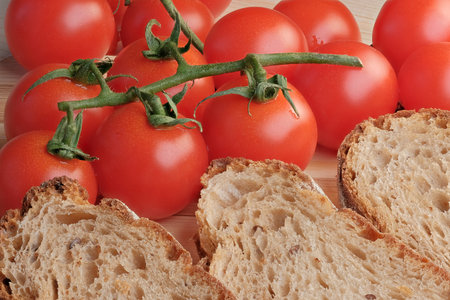 Small tomatoes on a twig lie on the table next to sliced whole grain hearth bread close-up macro...