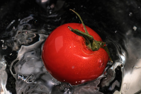 Red small tomatoes falling into a glass bowl with clean water for washing close-up macro photographyの写真素材