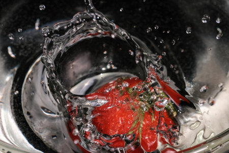Red small tomatoes falling into a glass bowl with clean water for washing close-up macro photographyの写真素材