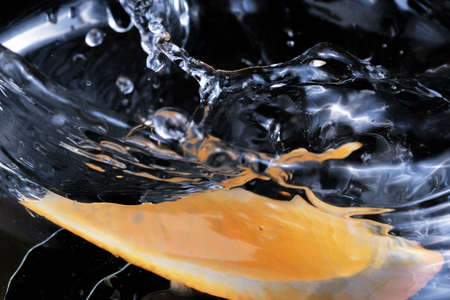 A slice of sweet ripe orange falls on a glass bowl with water close-up macro photographyの写真素材