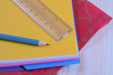 A stack of old tattered books in identical green bindings lies on a wooden table next to a notebookの写真素材