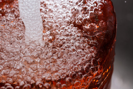 Abstract macro photography water in a powerful stream fills a red vase with the formation of air...