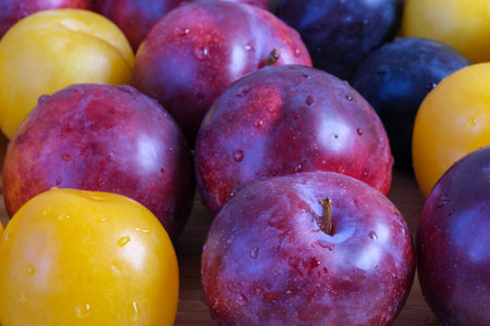 Multi-colored ripe sweet plums of different varieties on a wooden table close-up macro photography