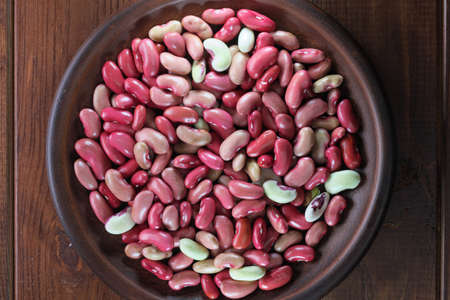 Fresh raw red beans in a clay plate on a brown wooden background close-upの写真素材
