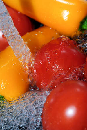 Multicolored bell peppers and red ripe tomatoes are washed in clean water close-up macro photography on a black backgroundの写真素材