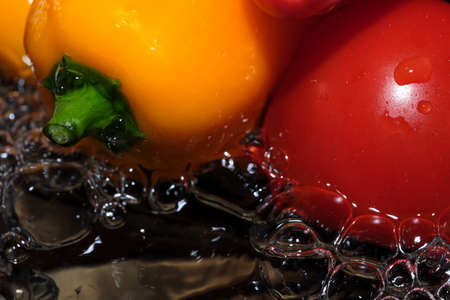 Multicolored bell peppers and red ripe tomatoes are washed in clean water close-up macro photography on a black backgroundの写真素材