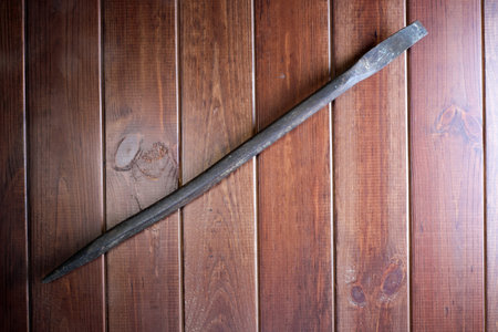 Old rusty locksmith pry bar on dark brown wooden background close-upの写真素材