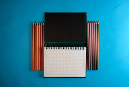 Tear-off notebook with colored pencils on blue paper background space for textの写真素材