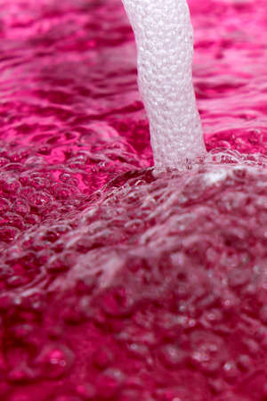 Abstract photograph of seething clear water flowing from a tap into a red container using ultra-short exposure close-upの写真素材